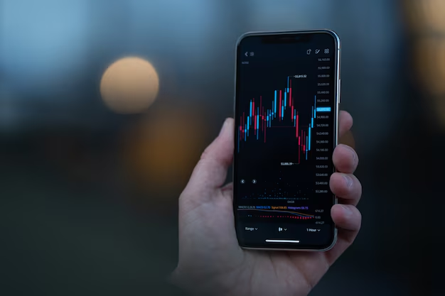Hand holding smartphone with trading chart interface showing candlestick patterns and market data